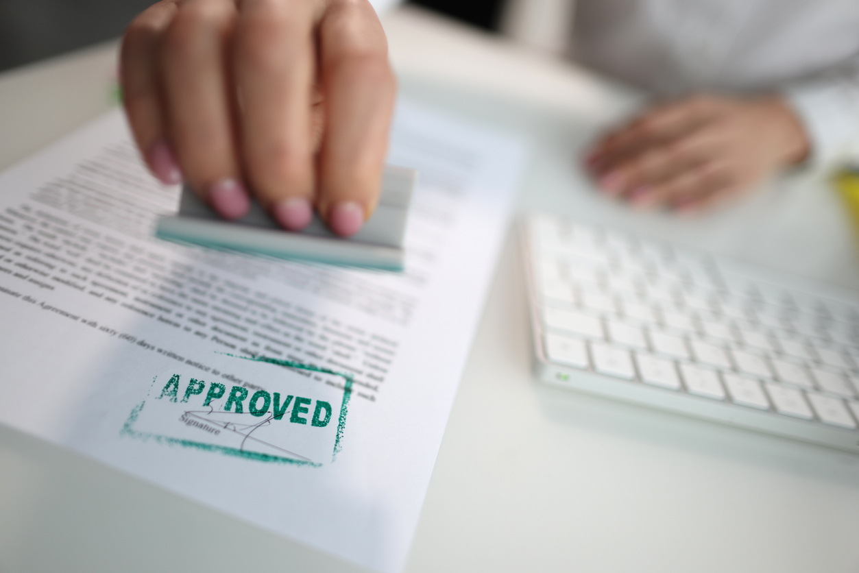 k-1 Visa application being approved, Closeup of a person hand stamping green approved seal on text approved document on table with 2 people