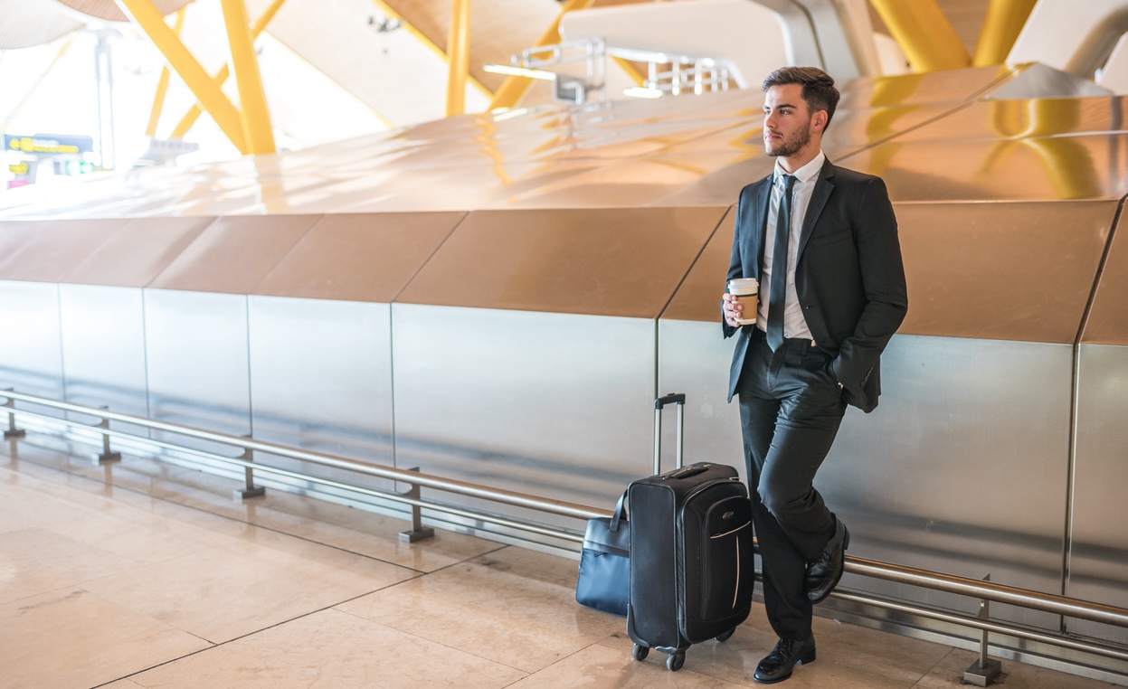 Hire a Chicago Business Immigration Attorney, happy businessman waiting in the airport with a coffee standing with luggage